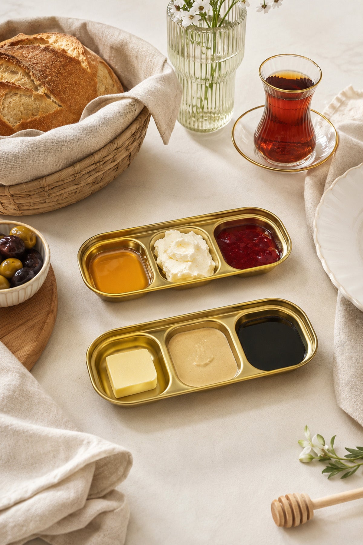 Altın renkli iki 3 bölmeli sunum kabında kahvaltılıklar, yanında ekmek ve çay