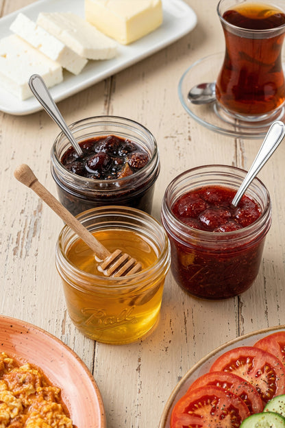 Çay ve peynirli kahvaltıda kaşıklı mini cam kavanozlarda bal ve reçel