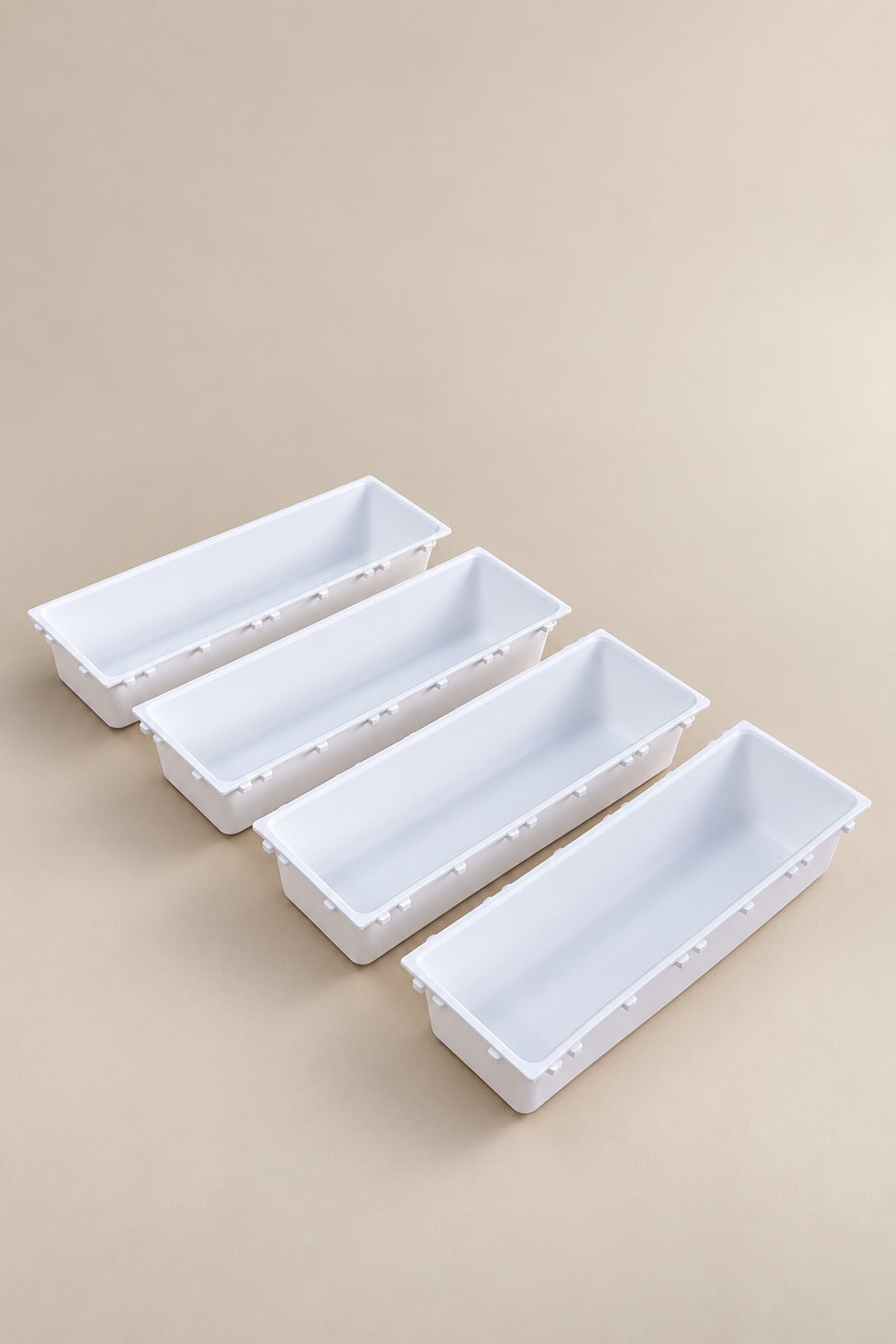 Bej zemin üzerinde yan yana dizili dört beyaz modüler çekmece düzenleyici kutu