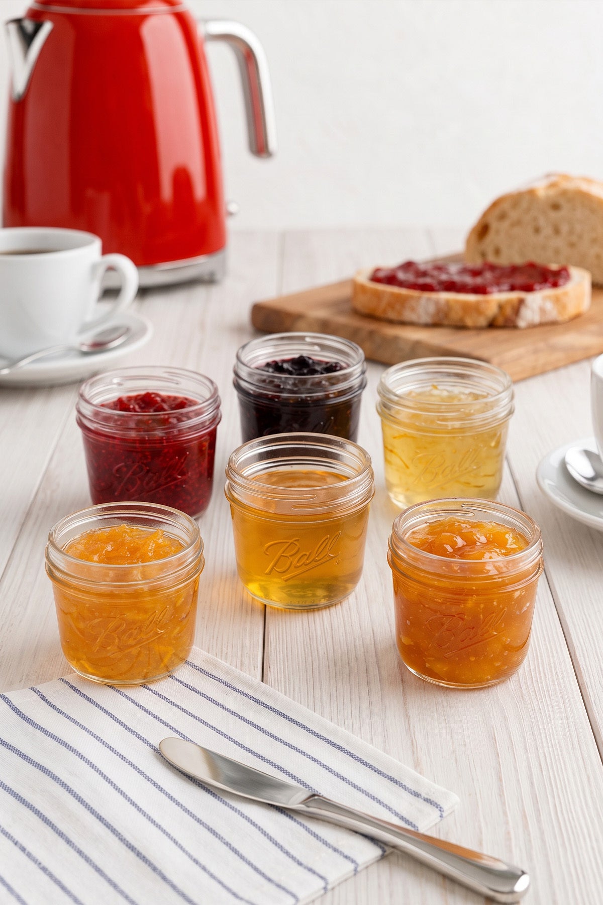 Kırmızı kettle önünde mutfak tezgâhında reçel dolu 100 ml cam kavanozlar