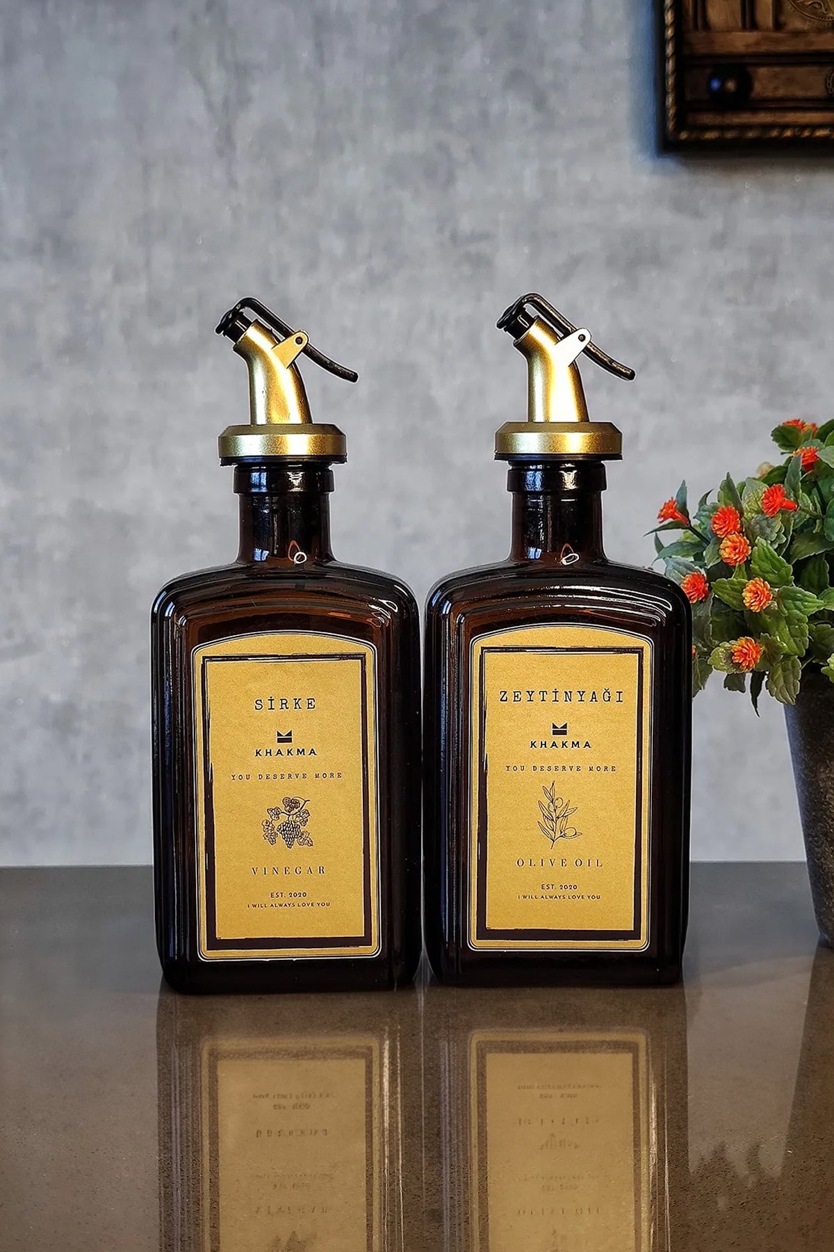Sirke ve zeytinyağı yazılı gold etiketli amber yağdanlıklar, yanında çiçek