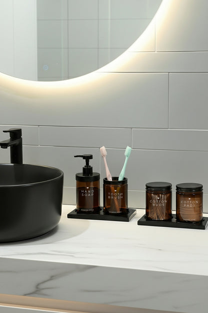 Işıklı ayna altında siyah lavabo yanında amber cam 4'lü banyo seti