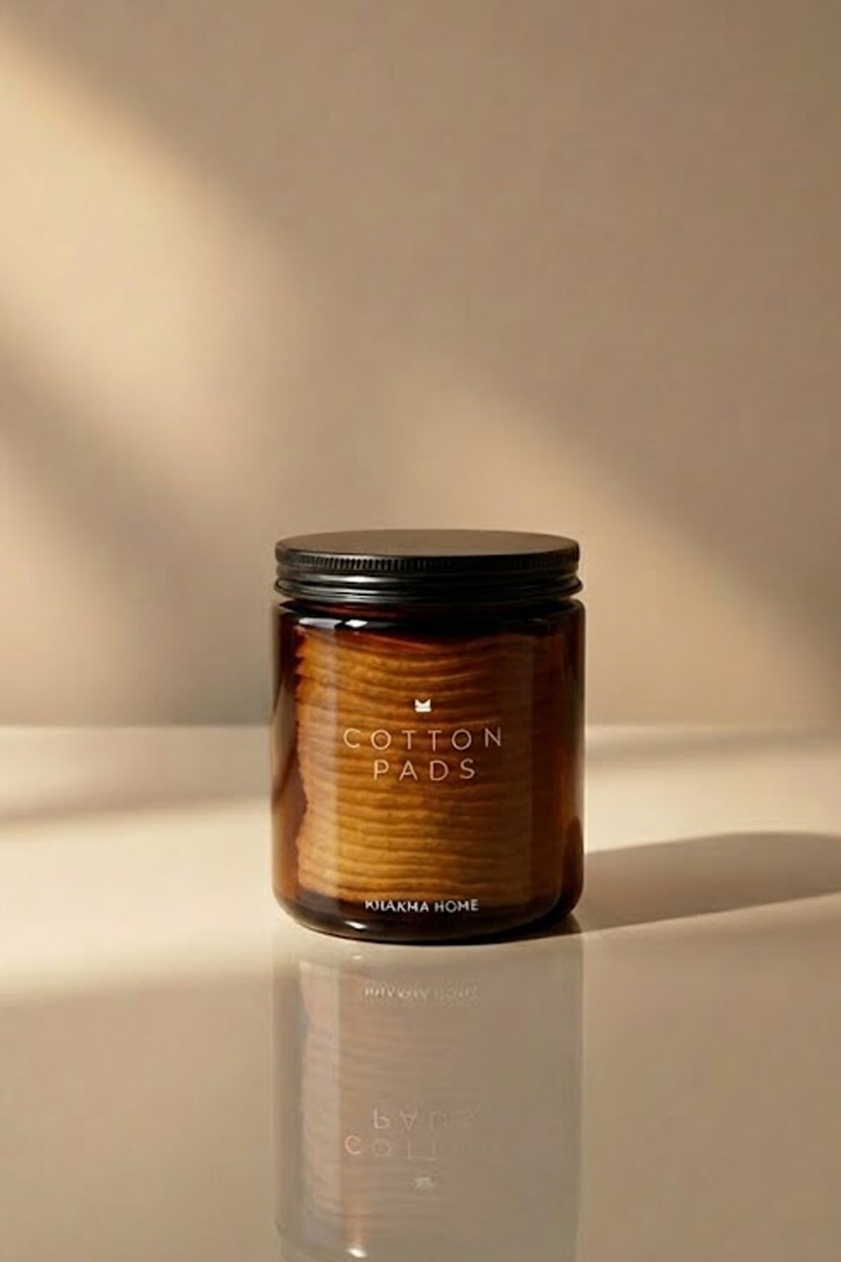 Makyaj pamuğu dolu, yansımalı zeminde duran amber cam Cotton Pads kavanozu