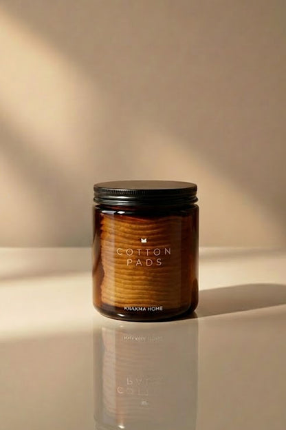 Makyaj pamuğu dolu, yansımalı zeminde duran amber cam Cotton Pads kavanozu