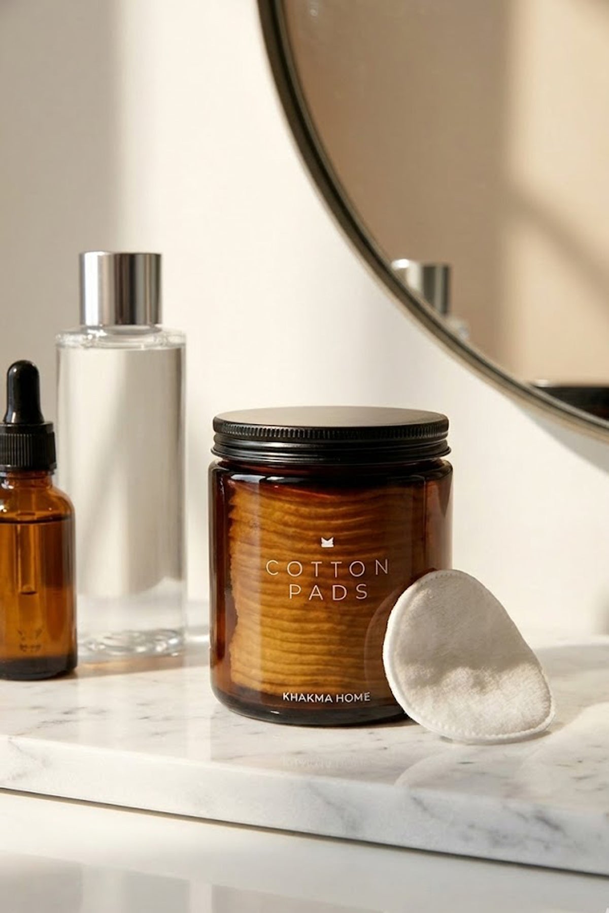 Aynalı makyaj tezgâhında serum şişeleri yanında amber cam pamuk kavanozu