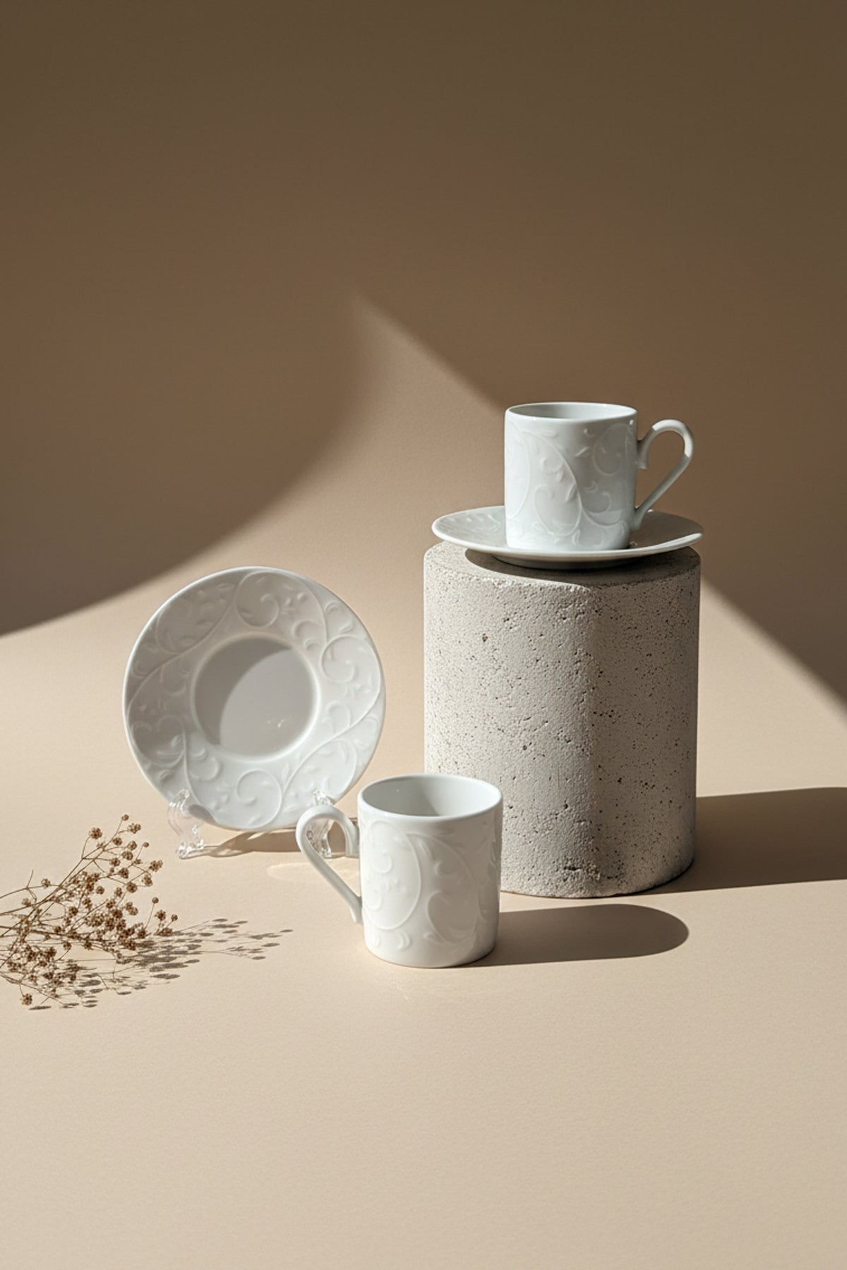 Beton kaide üzerinde kabartma desenli beyaz fincan, yanında tabak ve ikinci fincan