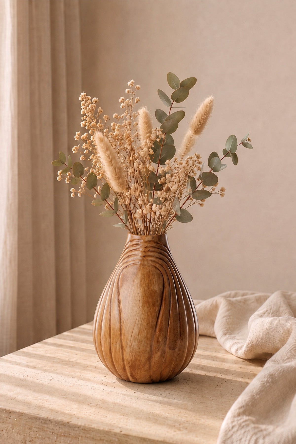 Travertin sehpa üzerinde kuru çiçekli kahverengi damla vazo, yanında örgü battaniye