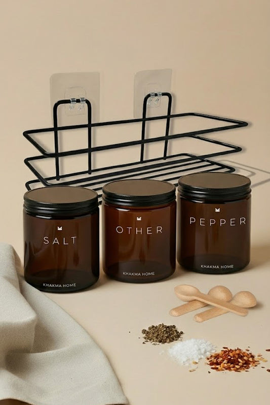 Siyah metal duvar standı önünde Salt, Other ve Pepper etiketli amber cam baharatlık kavanozları ve tahta kaşıklar
