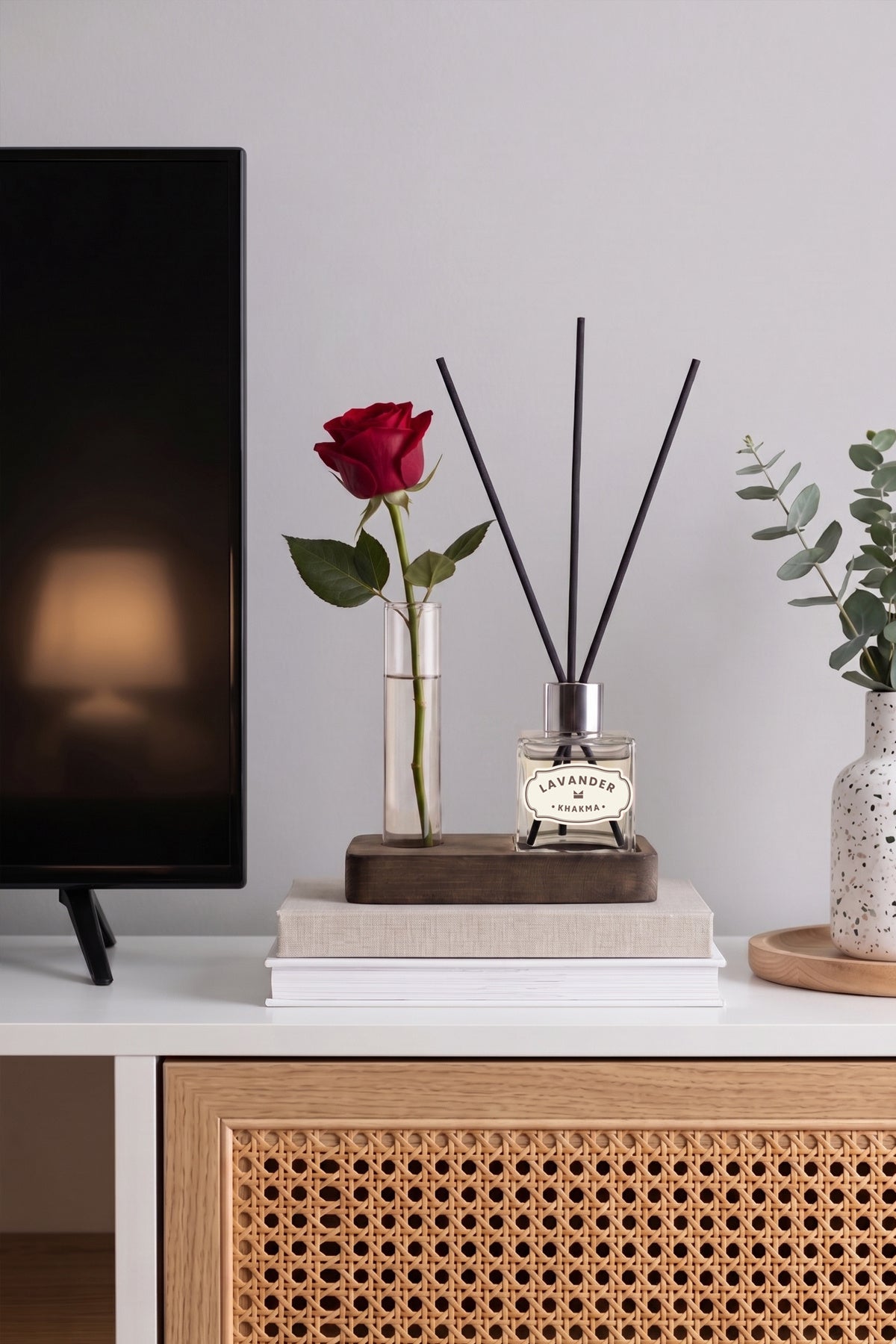 TV ünitesinde kırmızı gül konmuş vazo ile lavanta kokulu difüzör seti