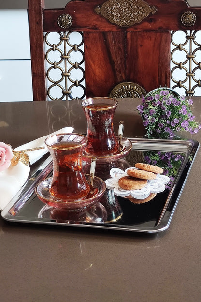 Ahşap sandalye önünde çay servisi yapılan parlak çelik sunum tepsisi