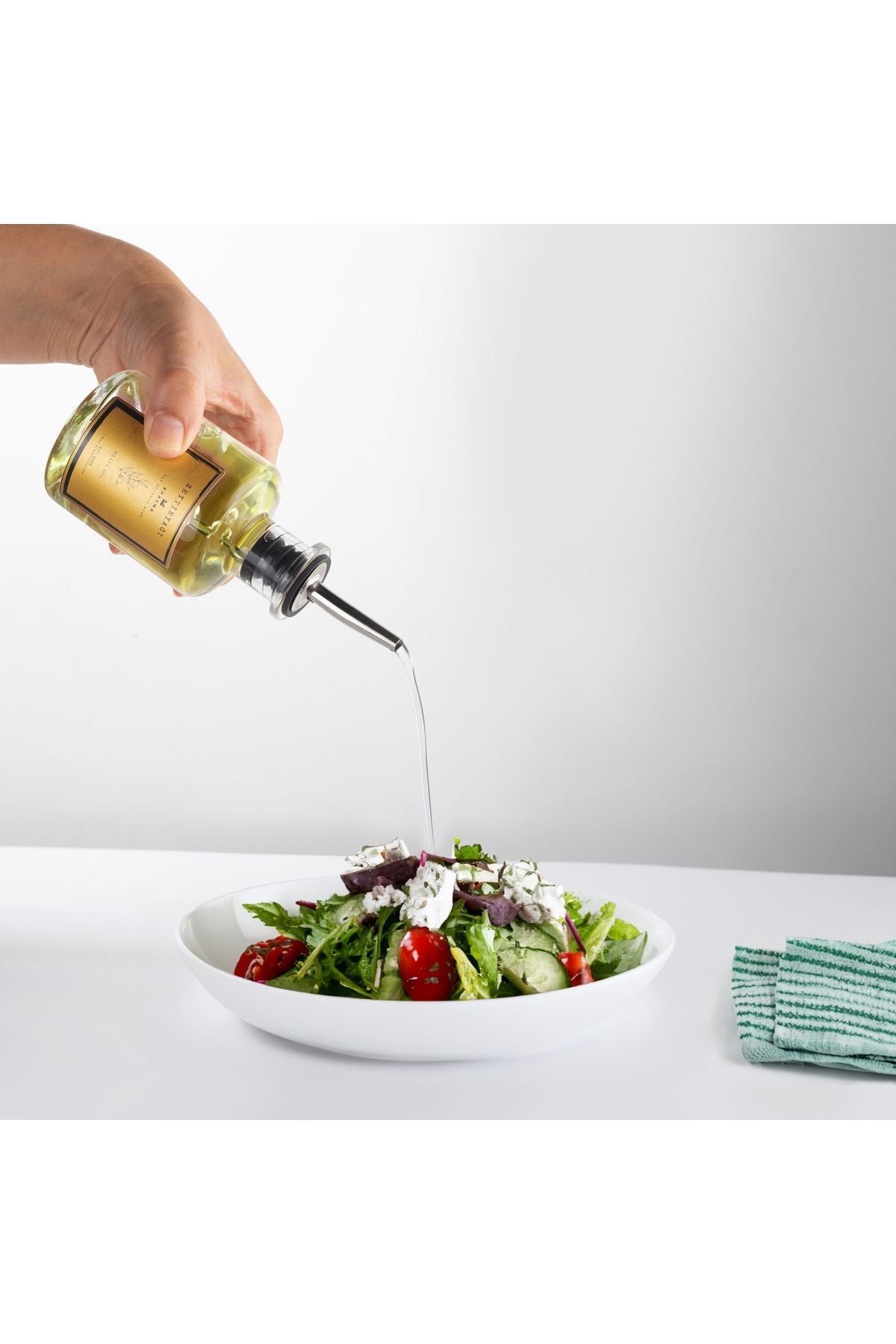 Çelik başlıklı şişeden salataya ince akışla dökülen zeytinyağı