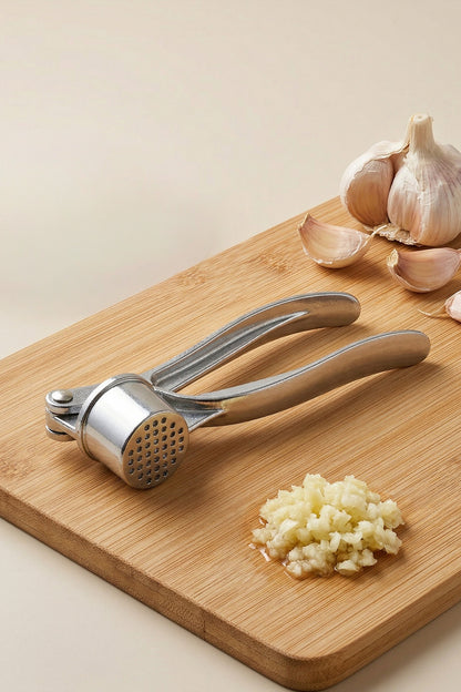 Bambu kesme tahtasında sarımsak dişleri ve ezilmiş sarımsak yanında metal pres