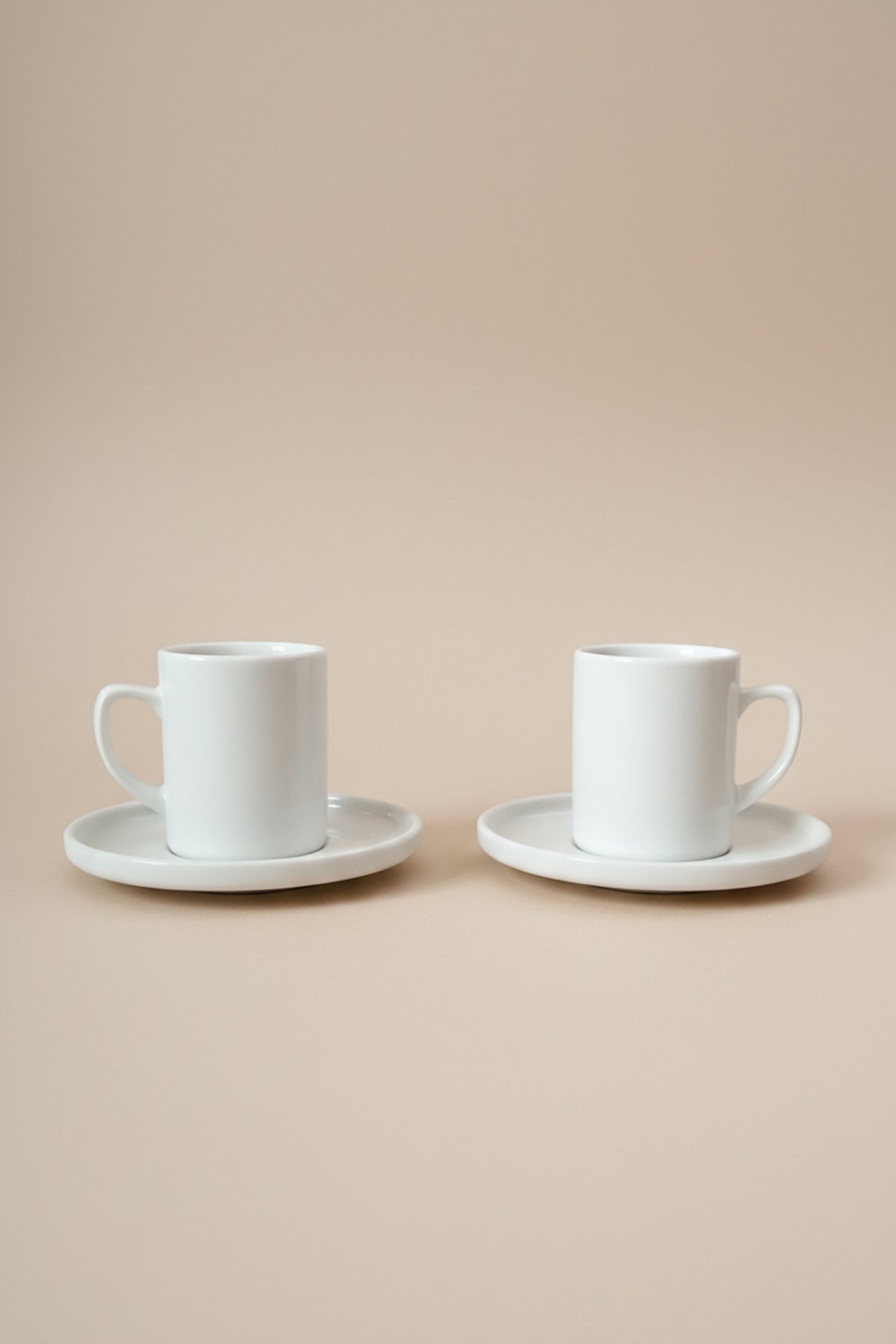 Yan yana duran 2 adet beyaz porselen Pure kahve fincanı ve alt tabakları