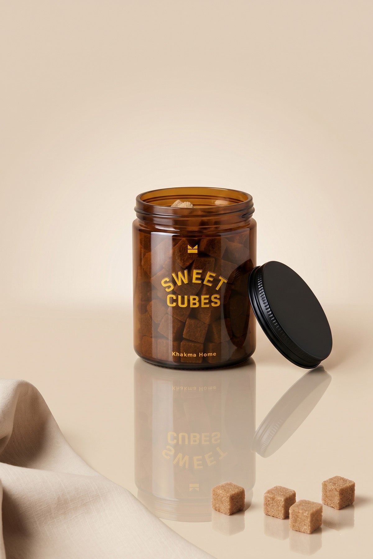 Kapağı açık Sweet Cubes amber cam kavanoz ve önünde esmer küp şekerler