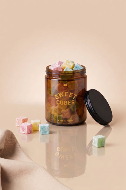 Renkli şekerlemelerle dolu, kapağı yanında duran 220 ml amber cam kavanoz