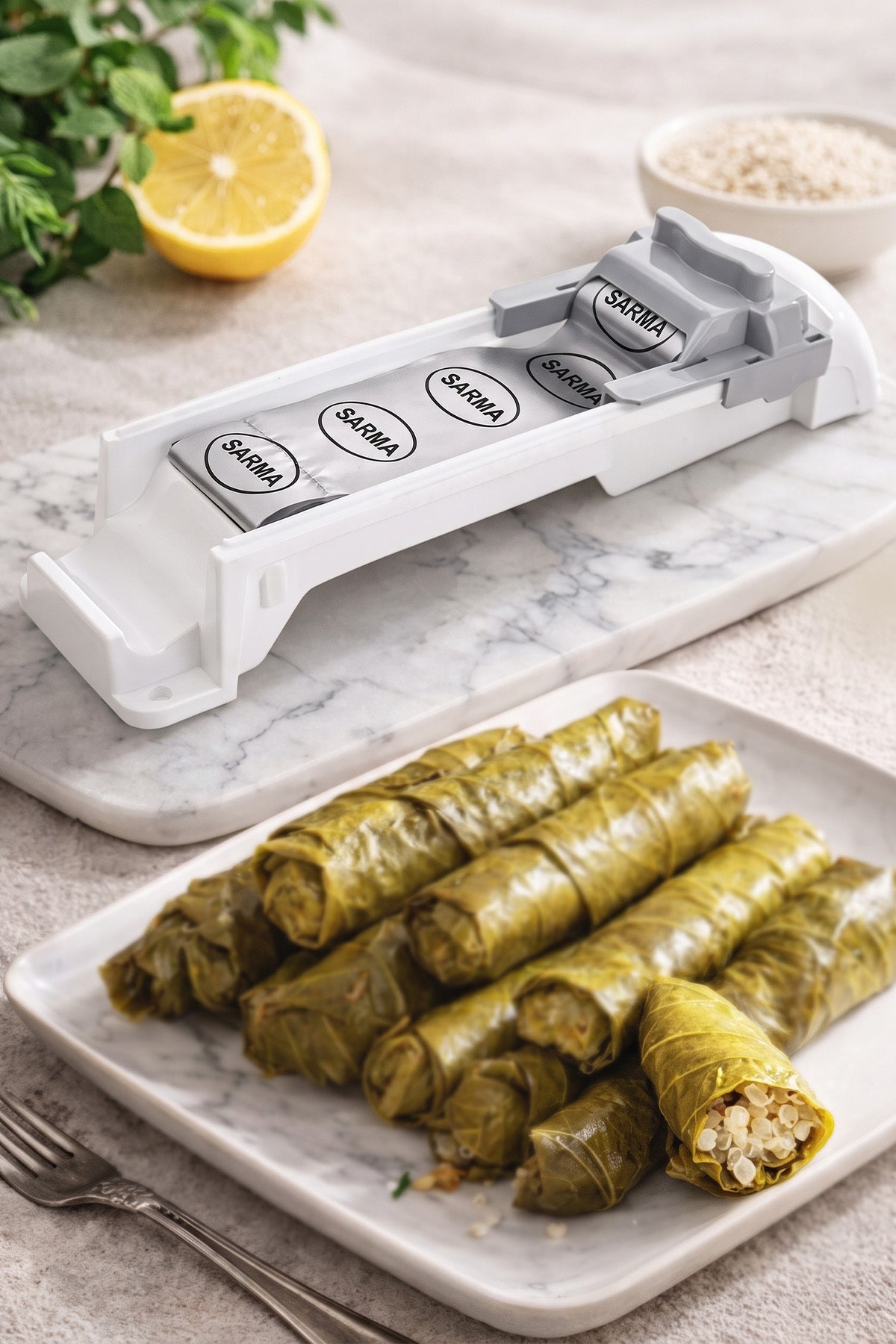 Mermer tezgâhta yaprak sarma makinesi ve önünde tabakta hazırlanmış eşit boyda sarmalar